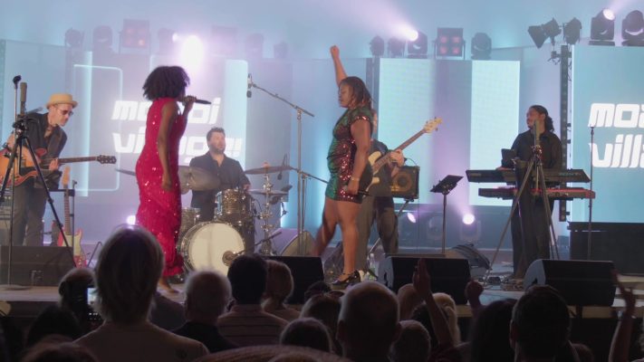 Moabi Village sur scène de nuit devant le public, la chanteuse lève le bras pendant le final
