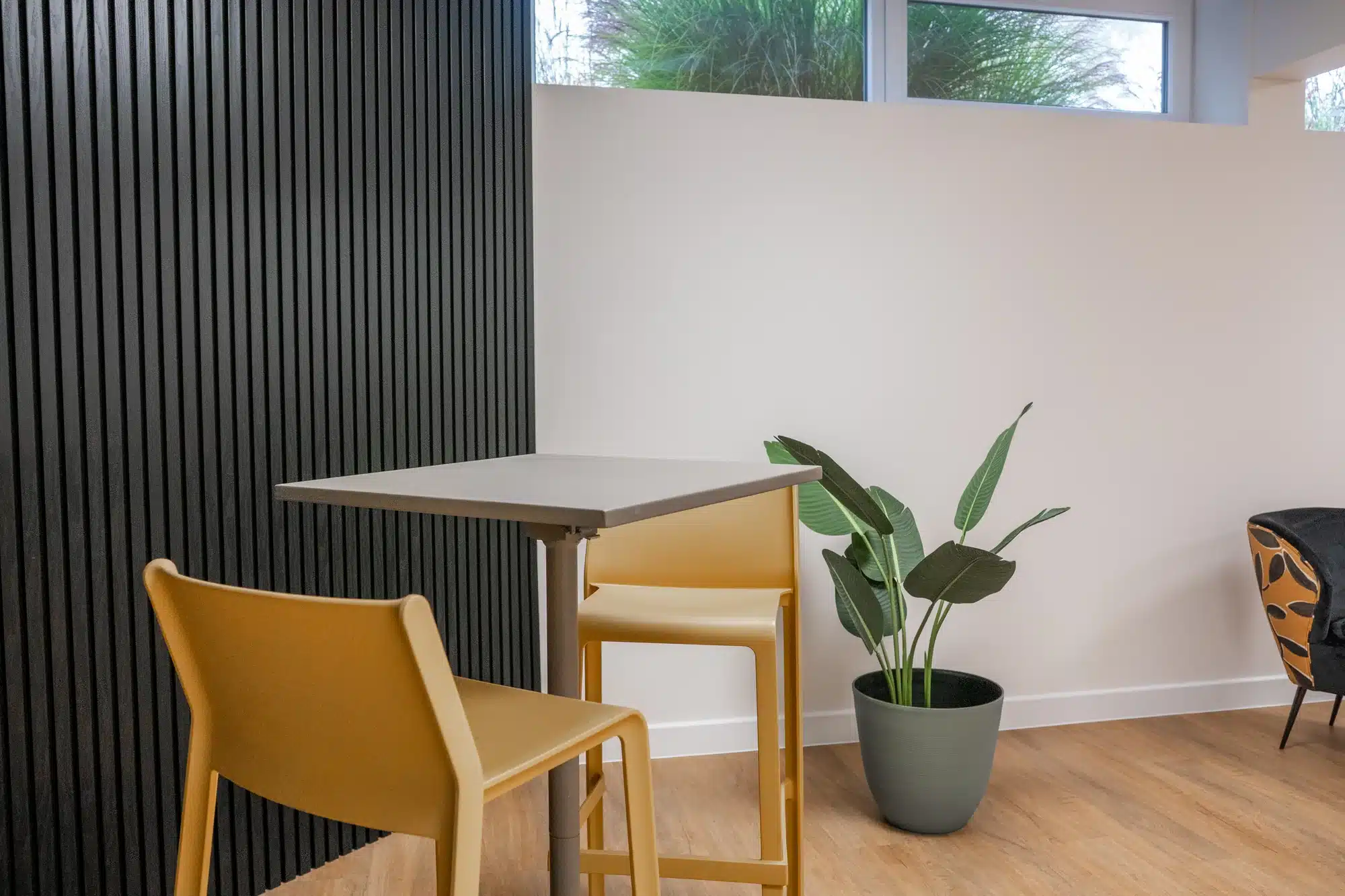 Espace de travail avec table haute, chaises jaunes et panneaux muraux.